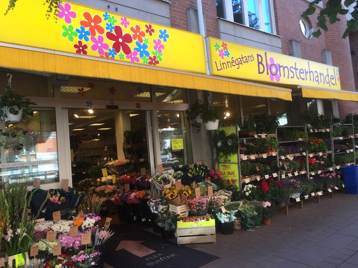 Butiken från sidan: gul markis med blomkonfetti, hyllor med krukväxter och buketter längs hela fasaden